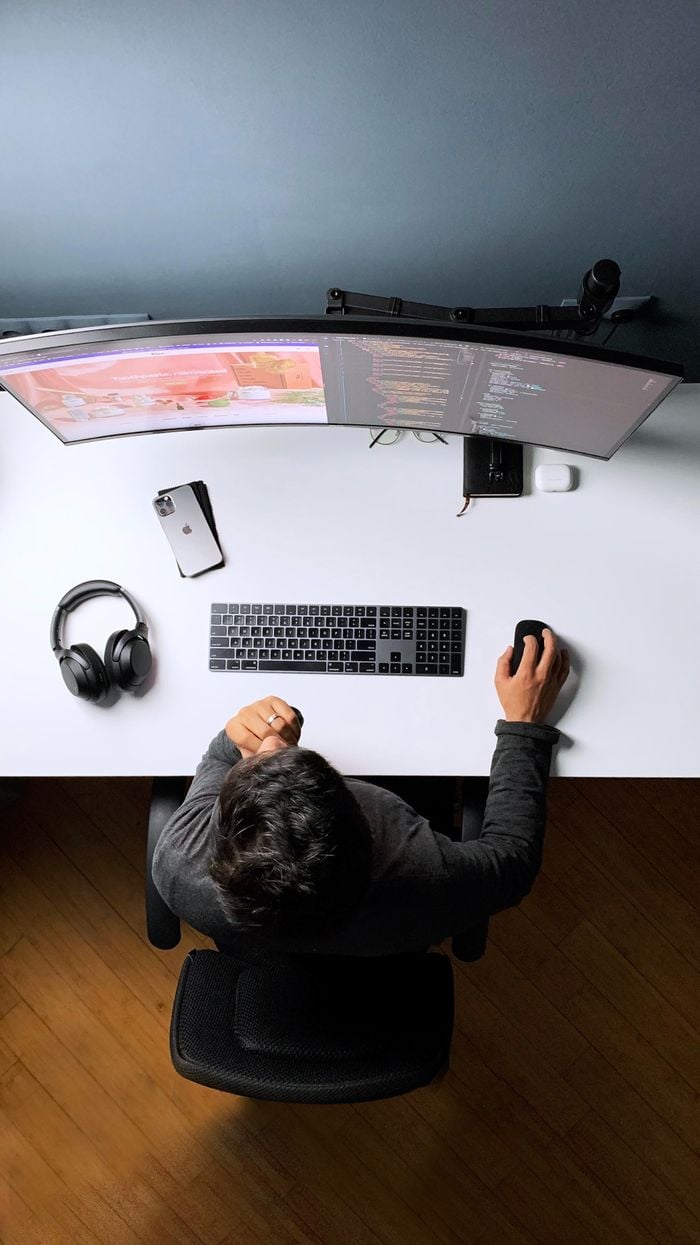Developer working at a desk with a widescreen monitor showing a website and code.